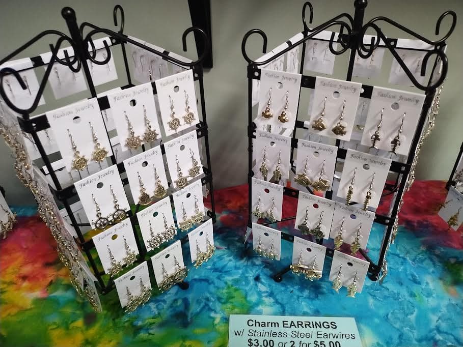 Two black metal racks displaying nautical charm earrings on white cards over colorful tie-dye fabric.