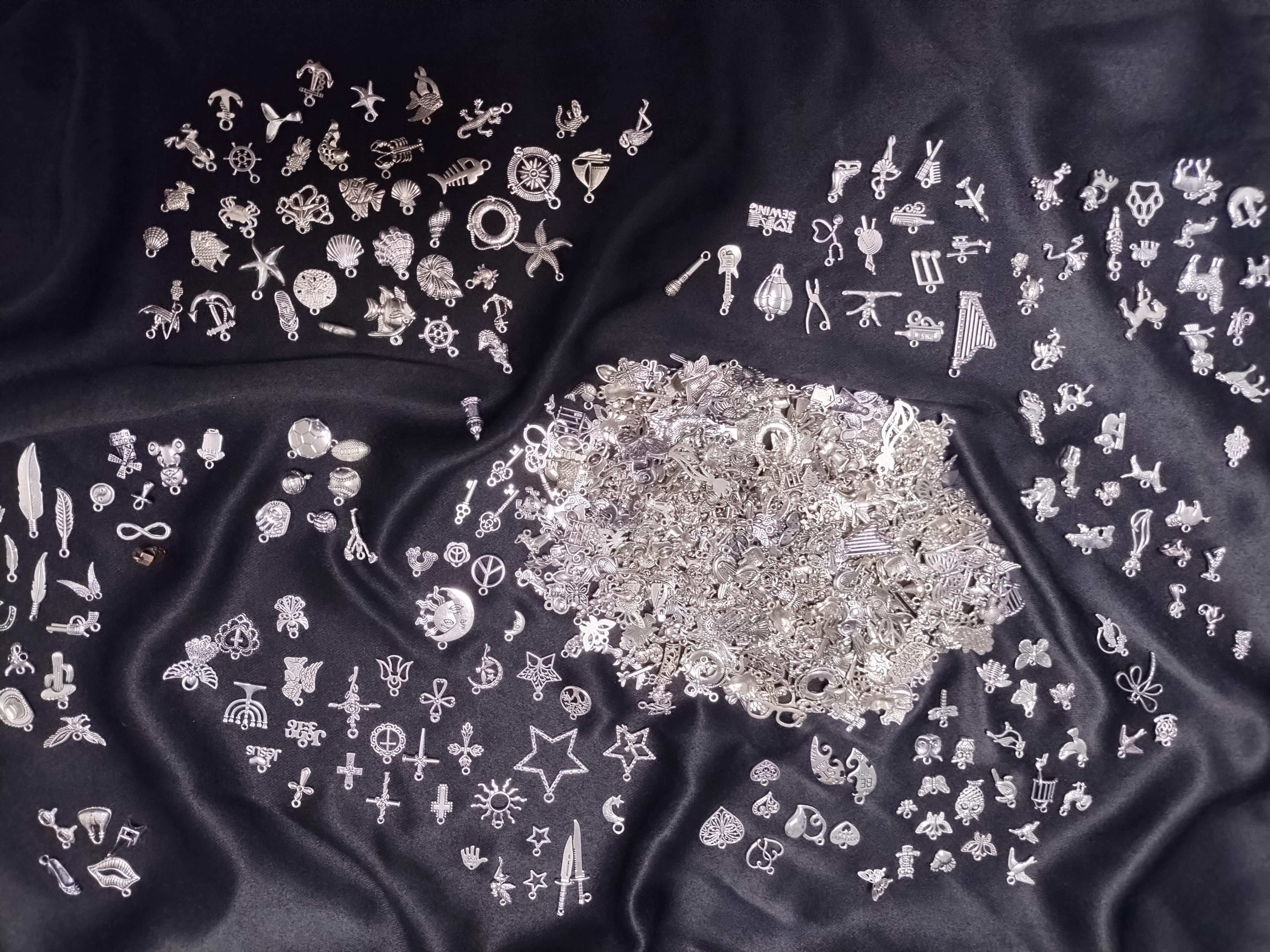 Diverse silver metal charms including animals, symbols, and objects scattered on black satin fabric.