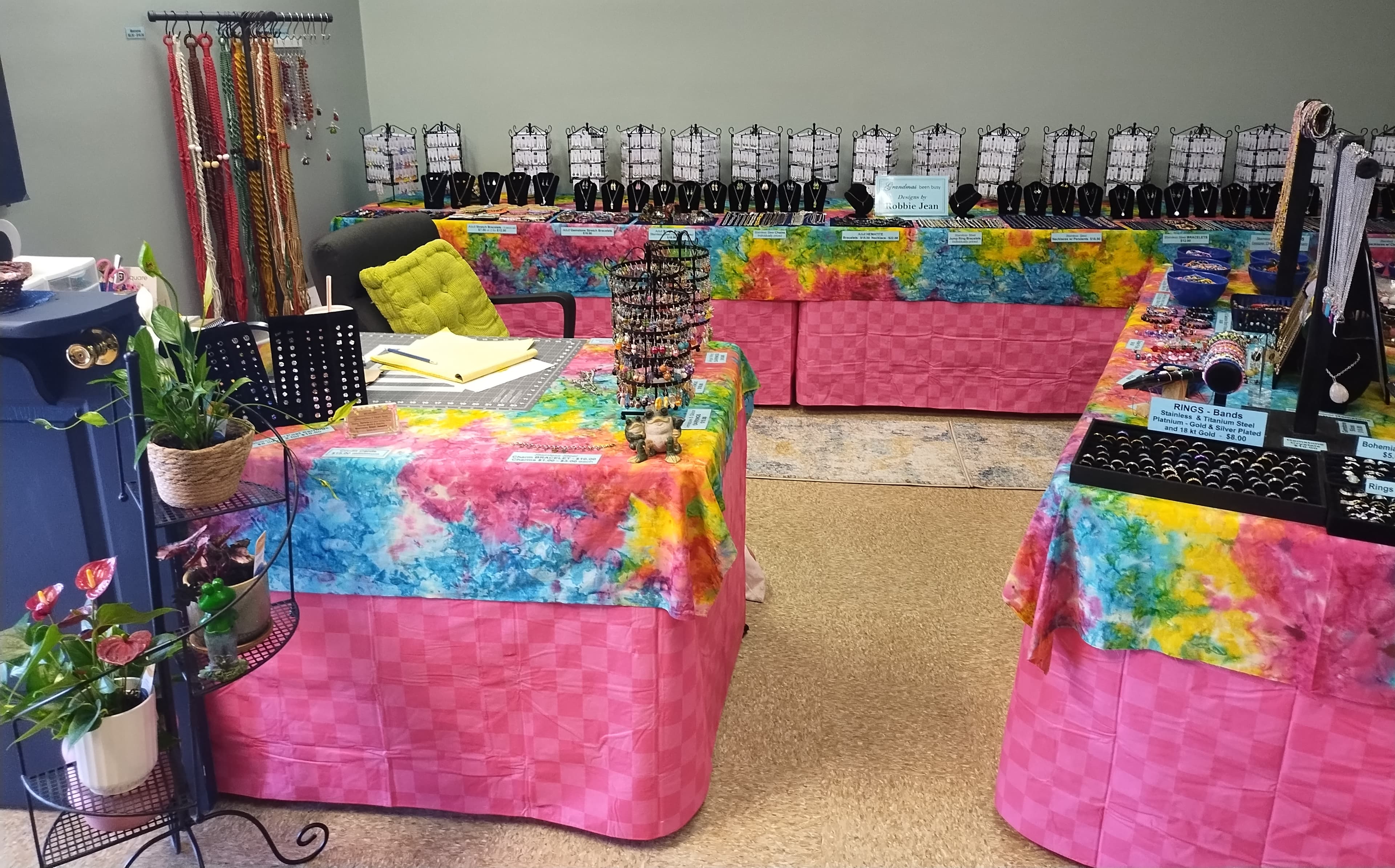 Jewelry display on tables with vibrant tie-dye cloths and pink checkered skirts.