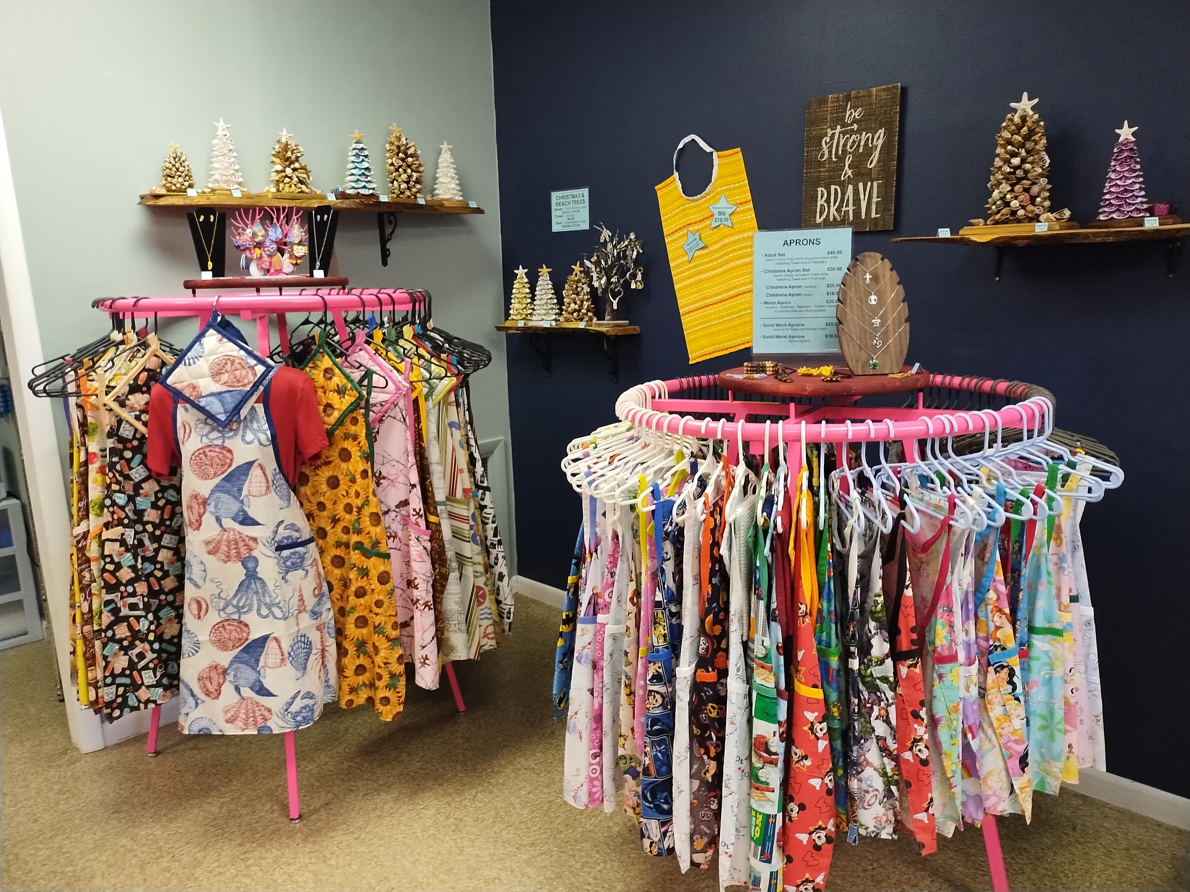 Colorful patterned aprons on circular pink racks in a boutique with decorative wall shelves.