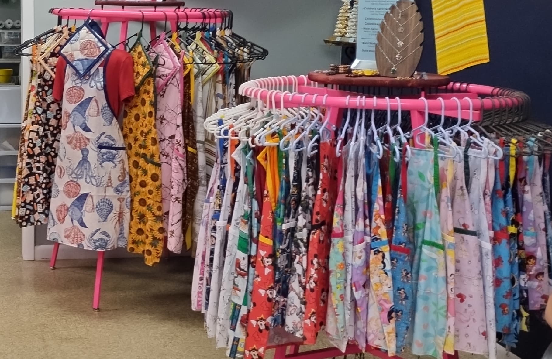 Colorful patterned aprons displayed on two pink circular clothing racks in a retail store.