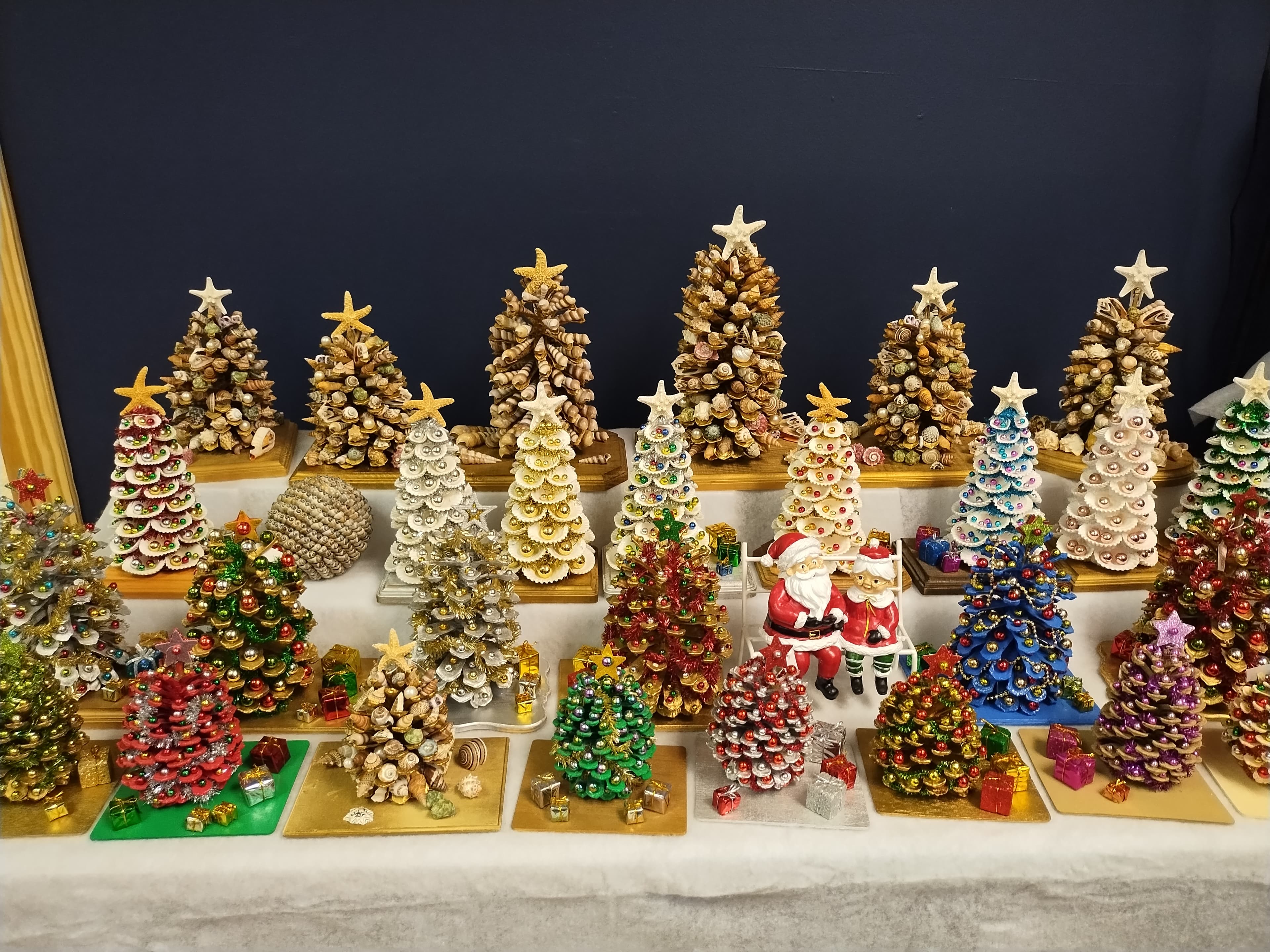 Miniature Christmas trees crafted from seashells and pinecones, decorated with colorful beads and stars.