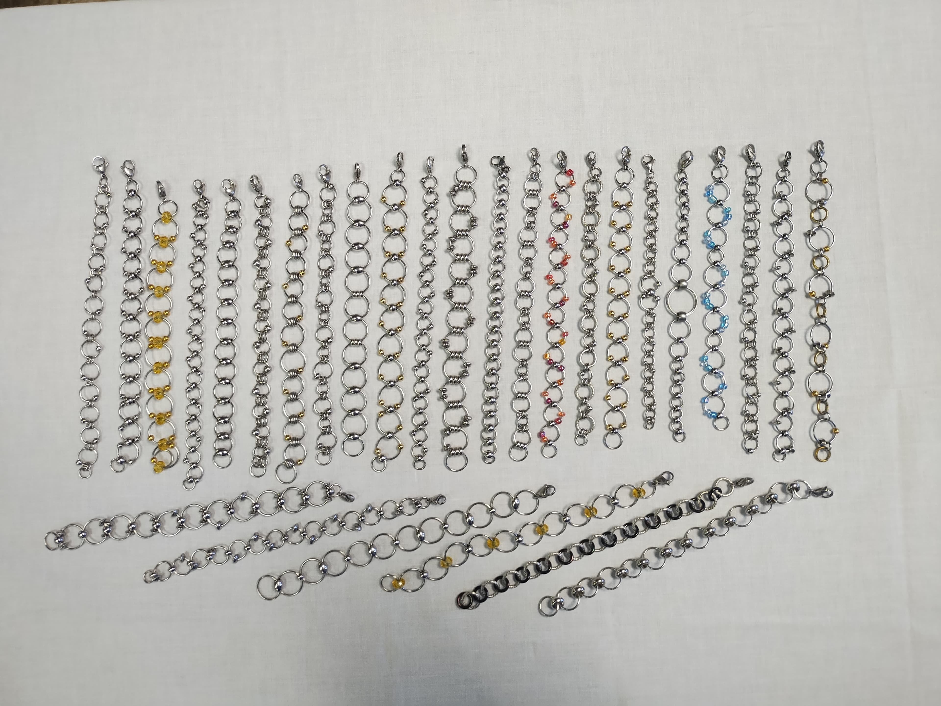 Silver chainmail bracelets and necklaces with colorful bead accents arranged on a white surface.
