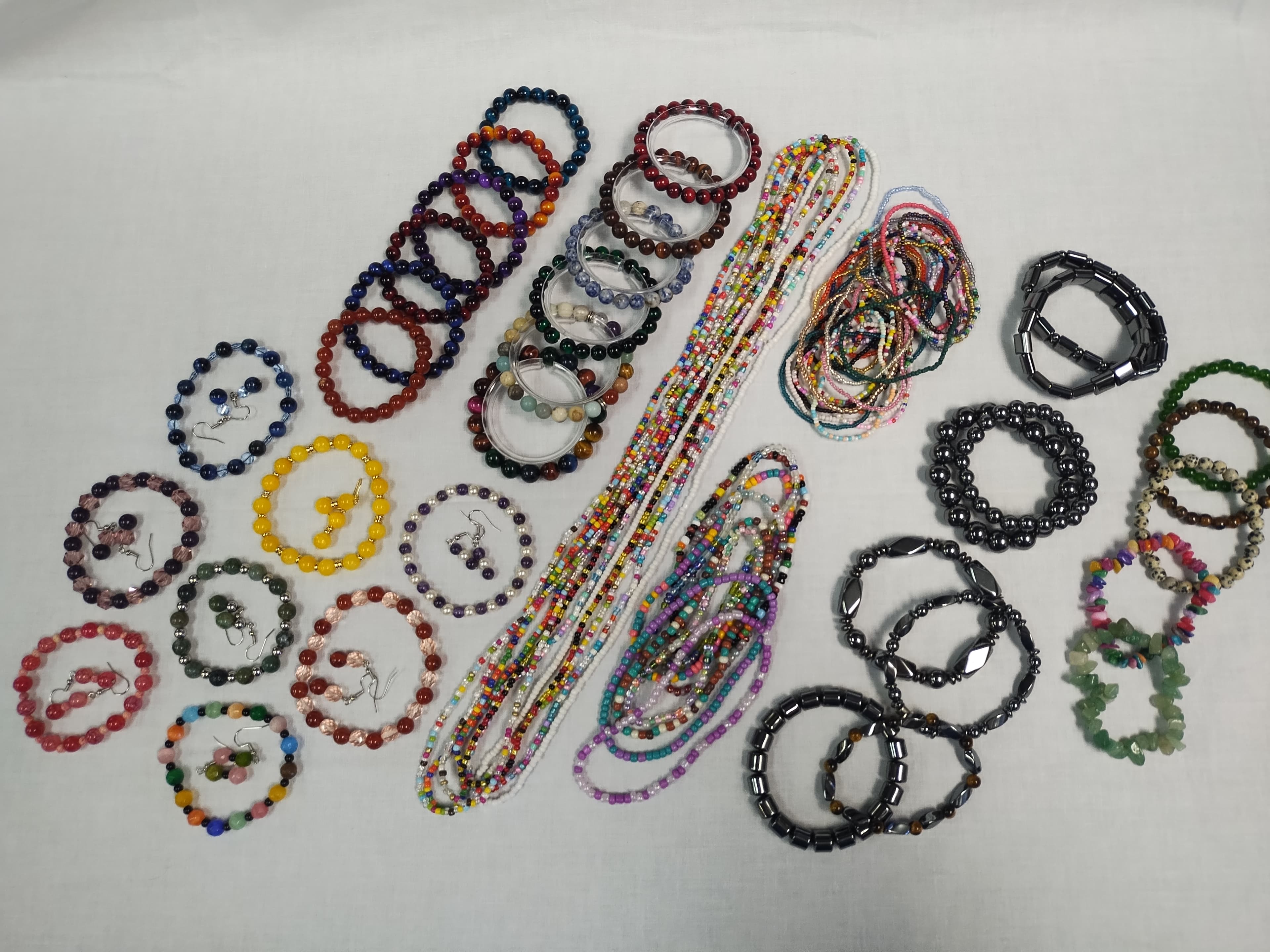 Assorted colorful beaded bracelets, matching earrings, and long seed bead strands on white.