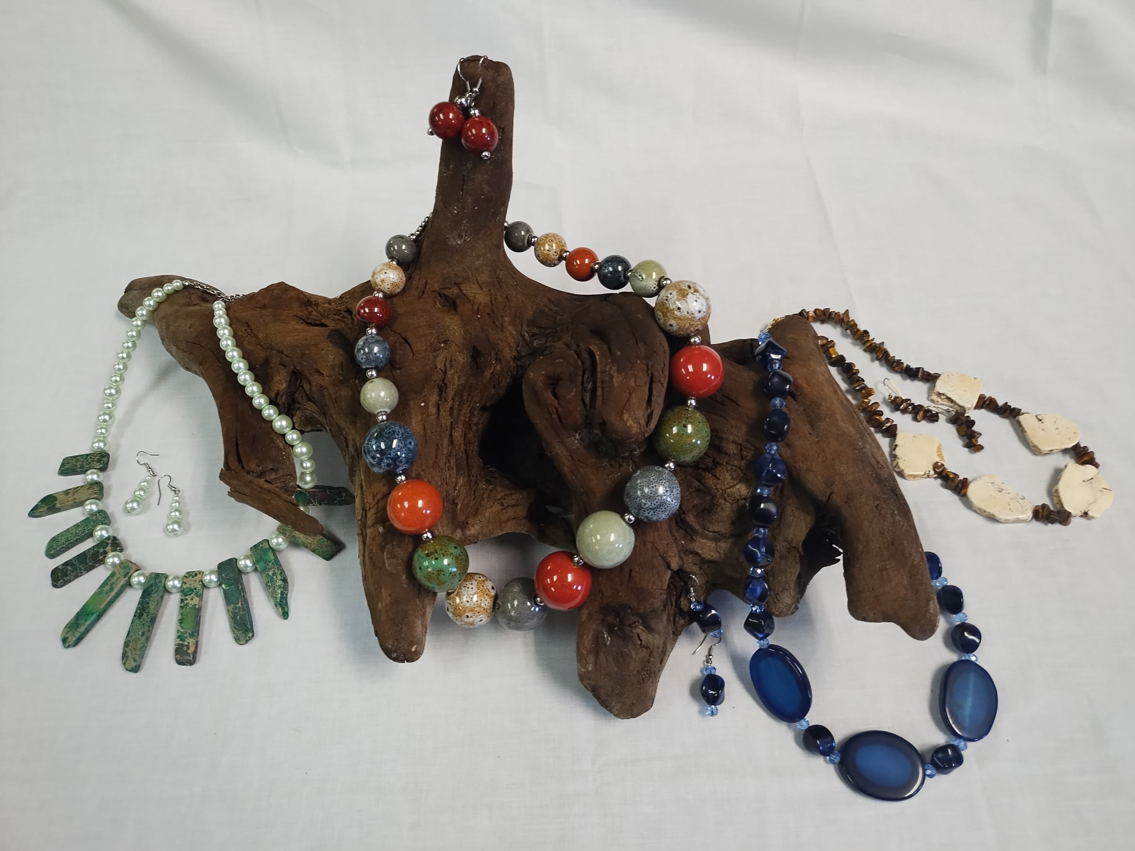 Multiple colorful beaded necklaces and matching earrings artistically displayed on a piece of dark driftwood.