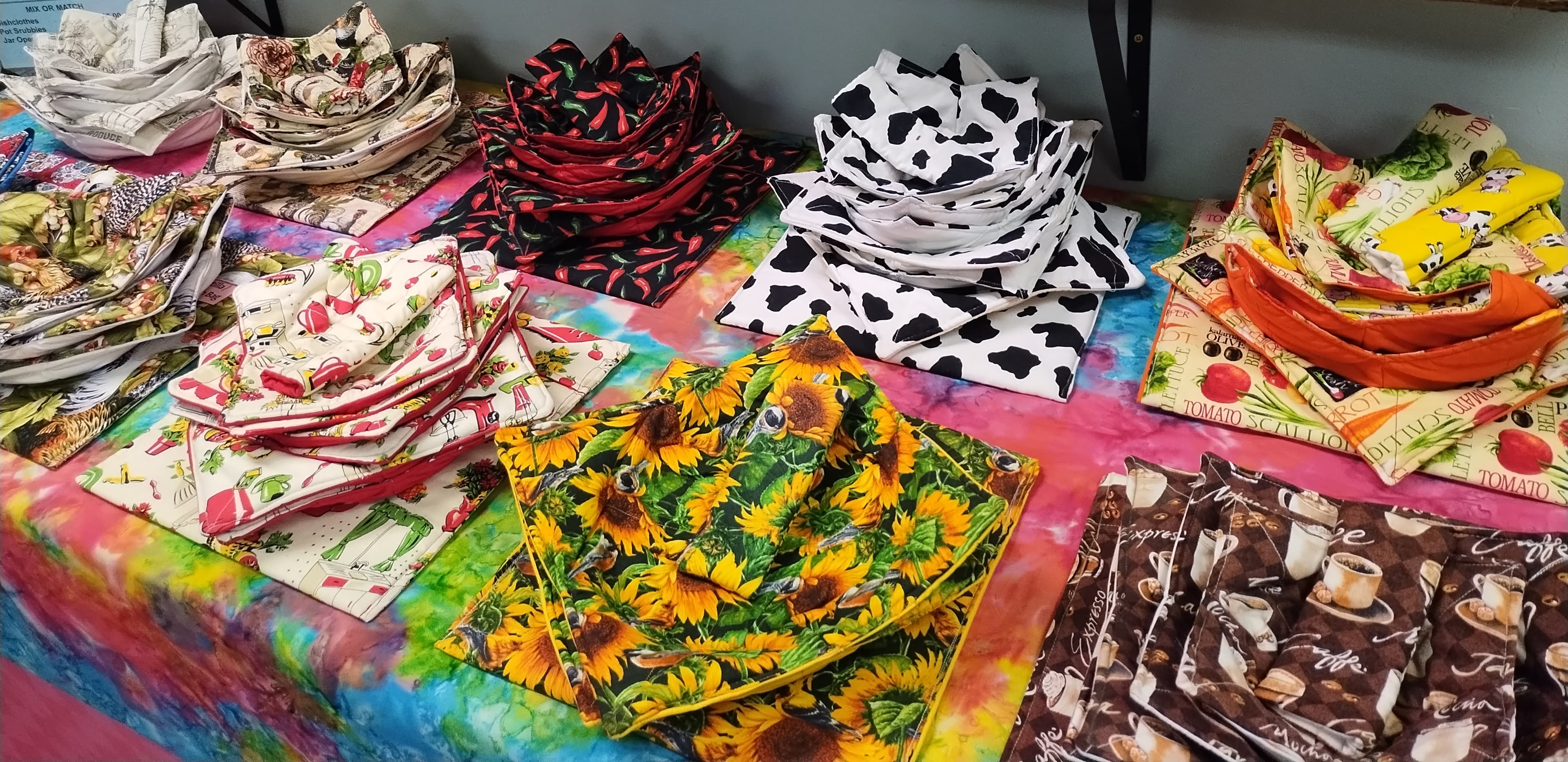 Handmade fabric bowl cozies in various patterns stacked on a vibrant tie-dye table cover.